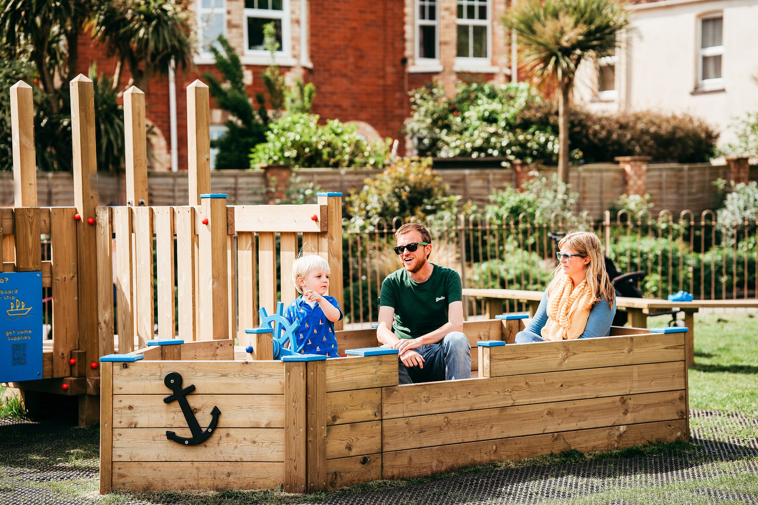 Family sitting in mini play boat whilst toddler stears the boat